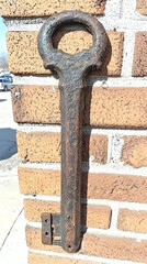 Rusty antique key on brick wall, outdoors, sunny day; historical artifact, decorative