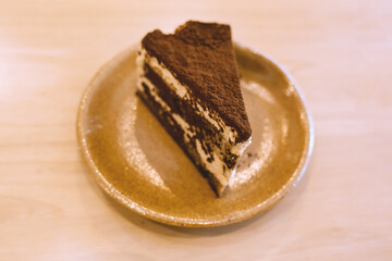 Slice of delicious tiramisu cake on ceramic plate served on wooden table in warm cozy cafe atmosphere
