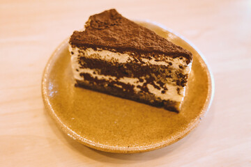 Slice of delicious tiramisu cake on ceramic plate served on wooden table in warm cozy cafe atmosphere