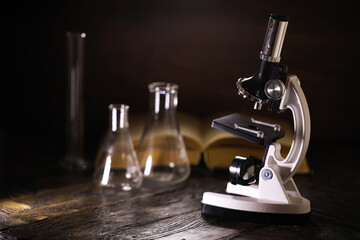 Laboratory Microscope and Glassware on Wooden Table with Open Book in Background - Science and...