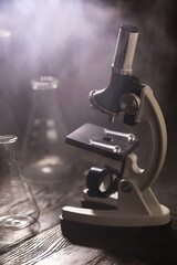 Vintage Microscope in a Foggy Laboratory Setting with Beakers and Dark Wooden Surface