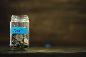 Clear Glass Jar Filled with Coins Labeled Donate on Wooden Background