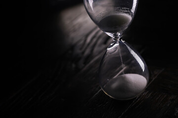 Elegant Glass Hourglass with Flowing Sand on Dark Wooden Background in Low Light