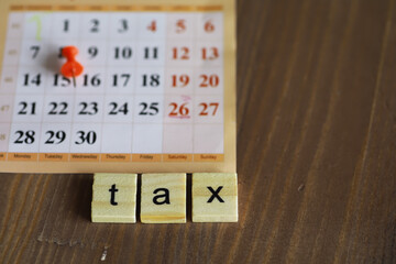 Tax Deadline Reminder with Calendar and Scrabble Tiles on Wooden Desk