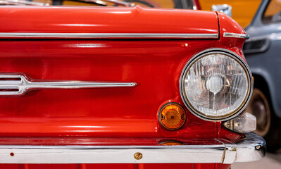 Close-up of the round headlights of a red classic car. Beautifully restored chrome parts of a...