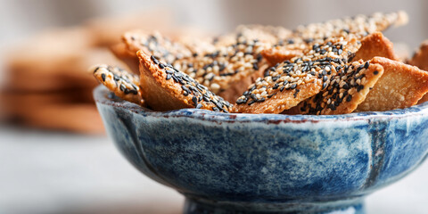 Close-up of sesame seed crackers in blue bowl, showcasing crispy texture and appetizing appearance, representing snack, food photography, or culinary concept