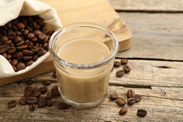 Coffee cream liqueur in glass and beans on wooden table, closeup