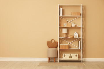 Shelving unit with decor, stool and wicker bag near beige wall indoors, space for text