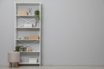 Different items on shelving unit near light grey wall. Space for text