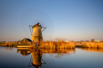 Traditional Dutch windmill reflecting on calm water during golden hour in the Netherlands.