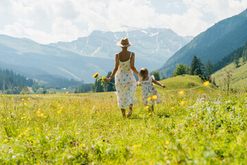 Fototapeta premium Mother and daughter spending time together in flower meadow outdoors. Mom and daughter in green nature at summer.