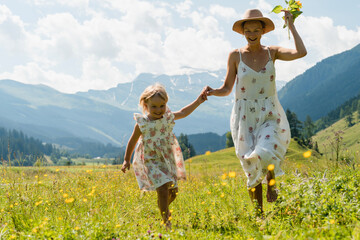 Mother and daughter spending time together in flower meadow outdoors. Mom and daughter in green nature at summer.