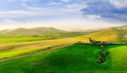 Obraz premium countryside sunset in green hills of spring fields with old castle farm and mountains on background of evening landscape