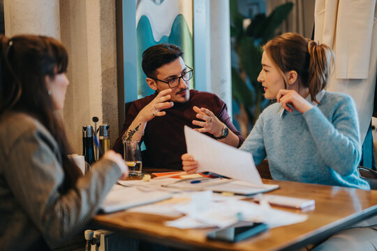 Three colleagues engage in an intense brainstorming session, discussing ideas during a planning meeting in a casual work environment, exhibiting teamwork, creativity, and focus.