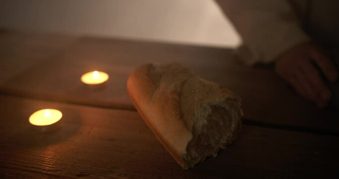 Jesus Christ hands on table with candles and passover bread for last supper or communion, as a representation of the Christian sacraments and Jesus as the bread of life, with ambient light.