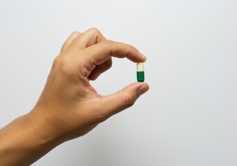 Fototapeta premium Hand holding a green and white capsule against a plain white background in a close up shot
