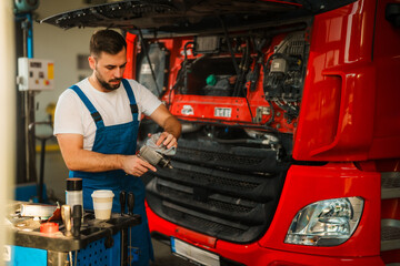 Mechanic in blue working suit work on a truck in a garage. The scene is well-lit with sunlight...