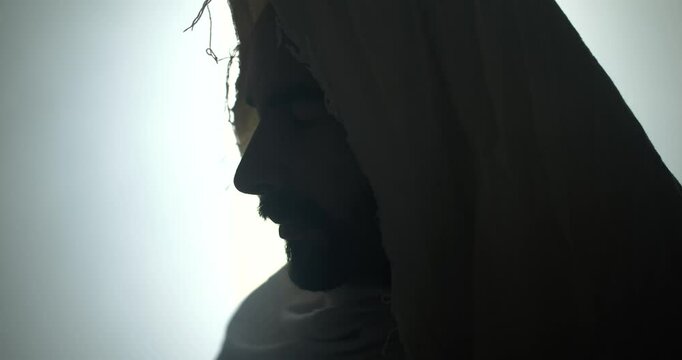 Closeup of the face of Jesus Christ in the tomb during Easter Sunday resurrection. Jesus closes his eyes in solemn prayer, worship, reflection in cinematic slow motion.