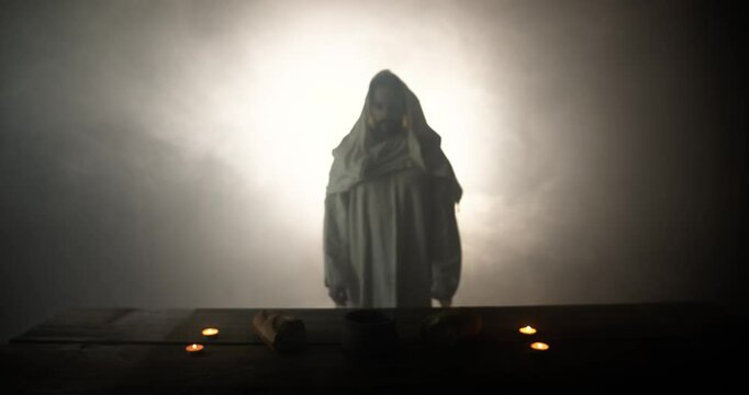 Jesus Christ walking to a table with Christian sacraments of bread and wine for last supper, communion, Easter symbolism. In cinematic slow motion with ambient light. Christianity visual.