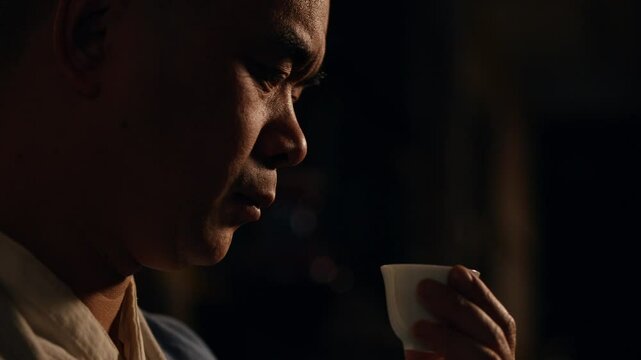 A man carefully examines a small tea cup, testing its contents, likely focusing on the taste or aroma