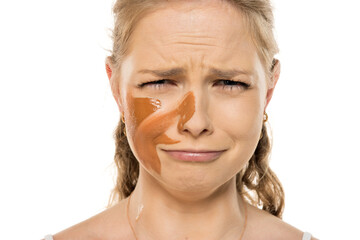 Young woman with worried, tearful expression showing distress over mismatched foundation streaks on...