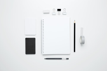 On a white background, an empty mock up notebook, white and black cards, and monochrome stationery...