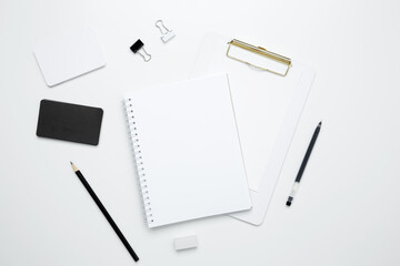 On a white background, an empty mock up notebook and clipboard, white and black cards, monochrome stationery items arranged neatly