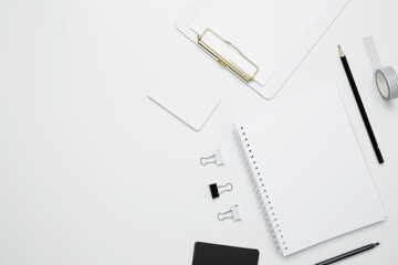 On a white background, an empty mock up notebook and clipboard, white and black cards, monochrome stationery items arranged neatly