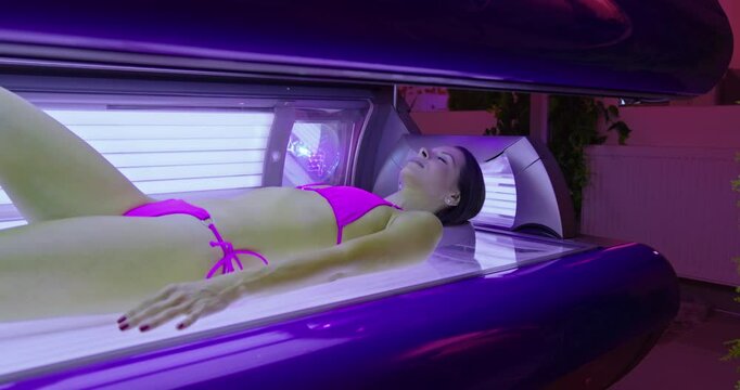 Young woman is lying on a tanning bed in a solarium and enjoying the artificial sunlight