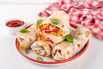 Homemade oven baked Pizza Burritos, pizza style quesadilla wraps with pepperoni or salami, tomatoes, cheese and corn, on kitchen table with hot tomato sauce, copy space