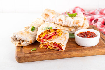 Homemade oven baked Pizza Burritos, pizza style quesadilla wraps with pepperoni or salami, tomatoes, cheese and corn, on kitchen table with hot tomato sauce, copy space