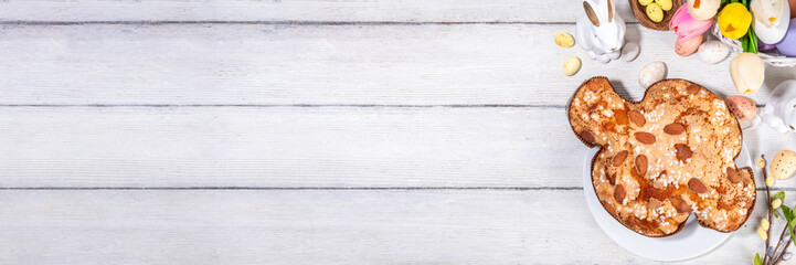 Italian Easter Colomba Cake, Colomba di Pasqua, sweet sugared dove-shaped sponge cake with glazed nuts and fruits, festive fruit- stuffed bread on white Easter holiday decorated table copy space