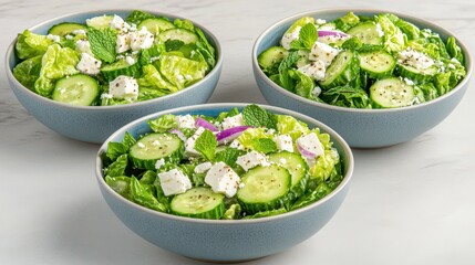 Obraz premium Fresh Garden Salad Bowls: Appetizing close-up of three vibrant salad bowls with cucumbers, fresh mint, and crumbled cheese arranged for a delightful and healthy meal experience.