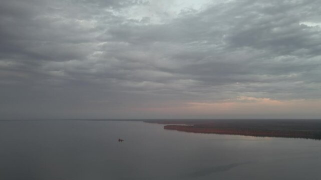 Drone aerial fling slowly above a large northern lake with a sky full of gray clouds
