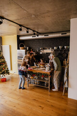 A big family of grandparents, parents, and children gathered in the kitchen to enjoy freshly baked homemade Christmas cookies. It creates a sense of warmth, festivity, care, and joyful moments.