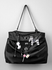 Close up of black fashion bag with funny keychains in the shape of horse, statue and lollipop