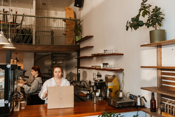 Two White adult women work inside a modern cafe during renovation. One stands behind the counter,...