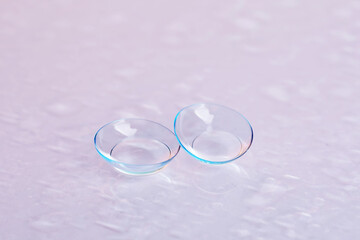 Pair of contact lenses and water drops on light mirror surface, closeup