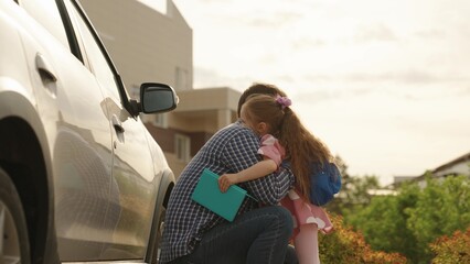 Happy family cute little daughter pupil and caring father embracing talking before primary school lesson outdoor. Smiling female kid child and dad hugging to each other going to elementary classroom