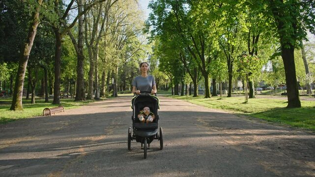 A young sporty woman walks in the park with her son in the running board. Mom is happy to do sports in the park with her newborn baby on a sunny day. Concept of power, fitness, family