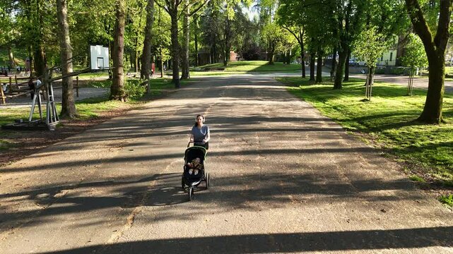 Aerial view of a sporty woman running with a stroller with a baby inside. Mom is free to do sports in the park on a sunny day. Concept of energy, fitness, family