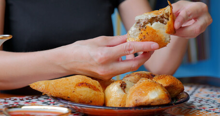 Woman breaks hot samsa in Uzbek cafe with colorful traditional setting.