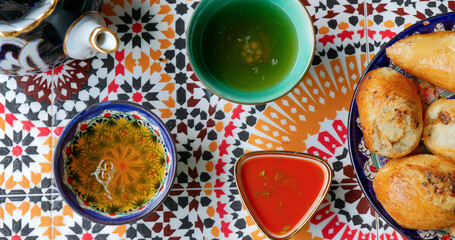 Plate of golden Uzbek samsa with red sauce and teapot on patterned table