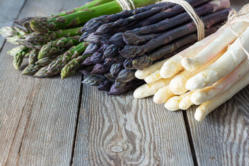 Raw white, purple, green asparagus on wooden background. Healthy food concept, place for copy...
