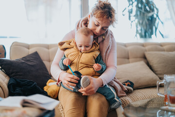 A tender moment of a mother holding her baby while seated on a couch in a warmly lit and cozy...