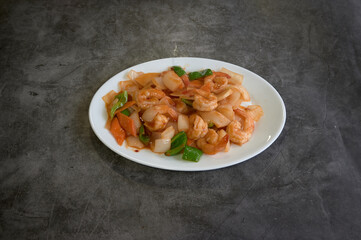 A plate of food with shrimp and vegetables. The plate is white and oval shaped. The food is on a grey surface