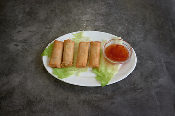 A white plate with four dumplings and a small bowl of sauce. The sauce is in a small bowl and is placed on the right side of the plate. The dumplings are arranged neatly on the plate