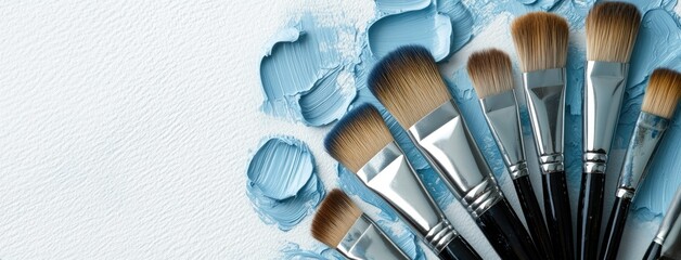 Various paint brushes arranged next to strokes of blue paint on textured white canvas in a creative workspace