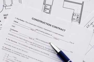 Pen on residential construction agreement and planning blueprints of residential building project