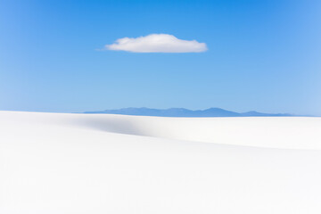 minimalist landscape featuring a vast expanse of white sand dunes under a clear blue sky. A single, fluffy white cloud floats above, adding a touch of softness to the scene